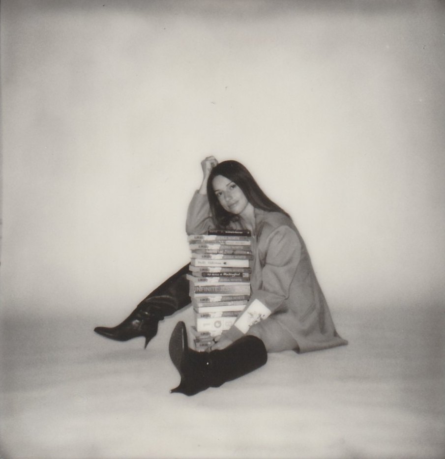 Jessa sitting on the floor with a stack of Liked between her boots
